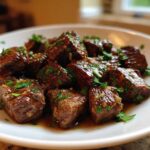 Close-up of tender, saucy crockpot steak bites seasoned and topped with fresh chopped parsley on a white plate.