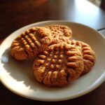 Close-up of four golden brown peanut butter cookies with classic crisscross fork marks, served on a white plate.