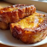 Two thick slices of perfectly cooked french toast stacked slightly, glistening with syrup.