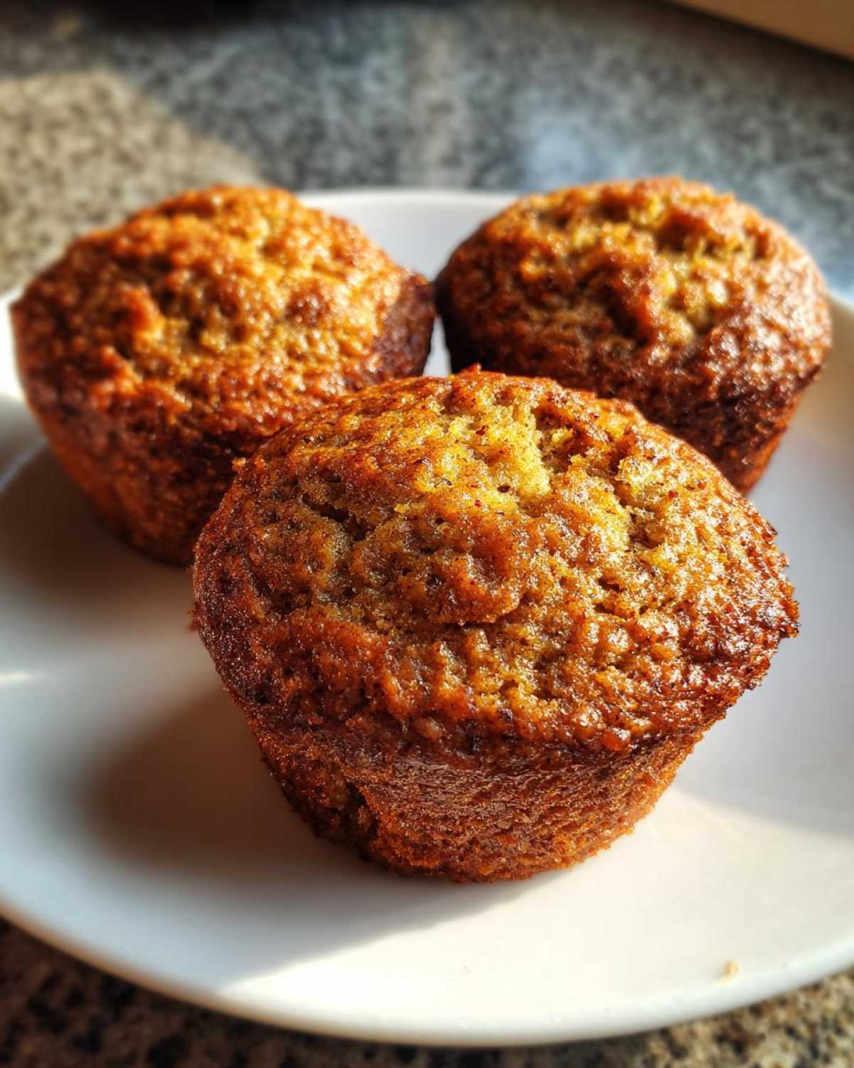 Three freshly baked, golden-brown honey bran muffins sitting closely together on a white plate.