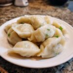 A close-up of freshly steamed Traditional Chinese Dumplings piled high on a white plate.