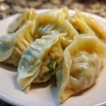 Close-up of freshly steamed Traditional Chinese Dumplings piled on a white plate, showing moist wrappers and green scallion filling.