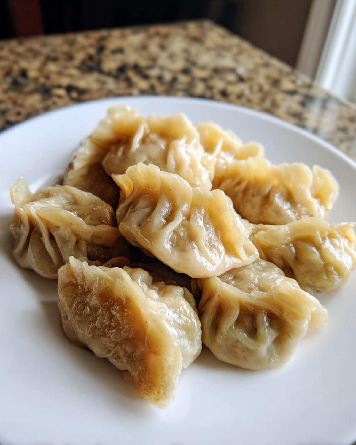 A close-up of several perfectly steamed Traditional Chinese Dumplings piled on a white plate.