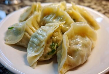 Close-up of freshly steamed Traditional Chinese Dumplings piled on a white plate, showing moist wrappers and green scallion filling.
