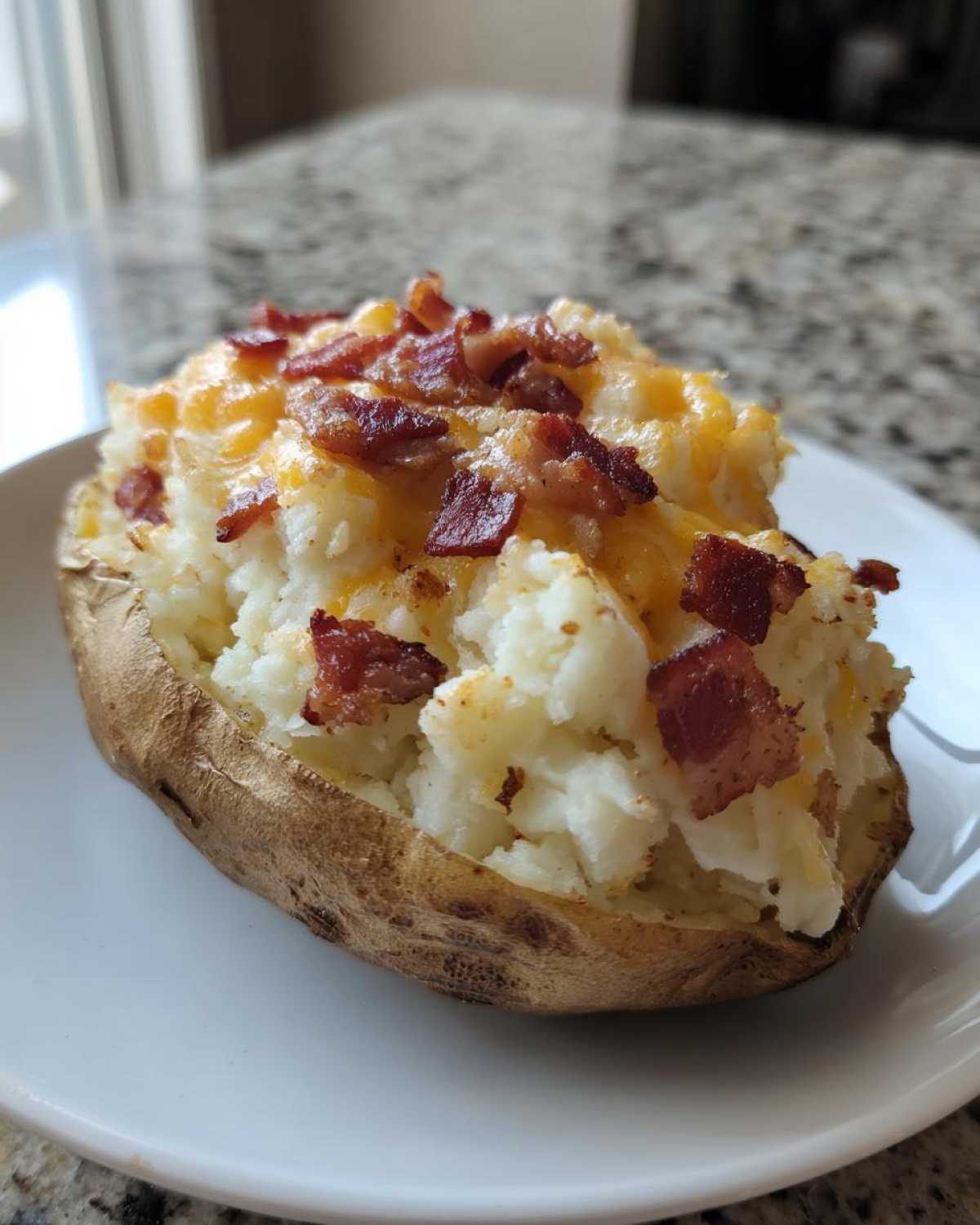 A close-up of a perfectly loaded twice baked potato stuffed with mashed potato, melted cheddar cheese, and crispy bacon bits.