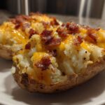 Two halves of twice baked potatoes stuffed with creamy filling, topped with melted cheddar cheese and crispy bacon bits.