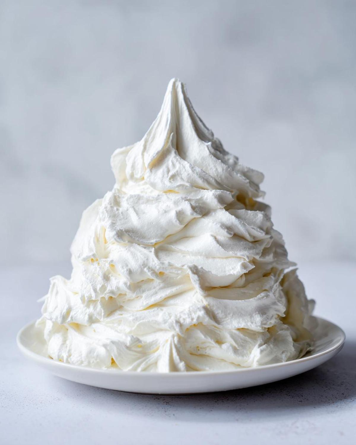A large, peaked mound of perfectly whipped vanilla buttercream frosting sitting on a small white plate.