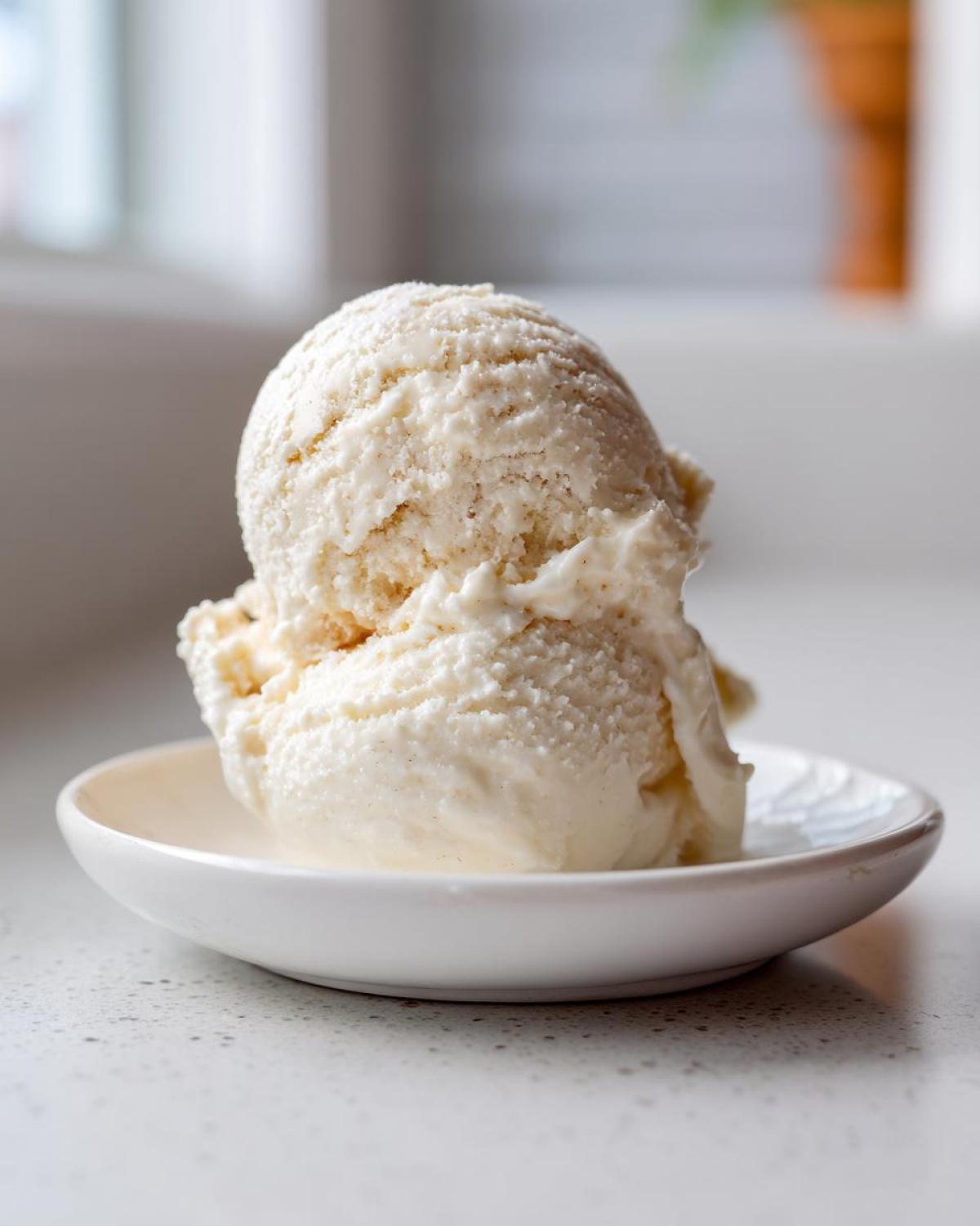 Two scoops of creamy vanilla cottage cheese ice cream served on a small white saucer.
