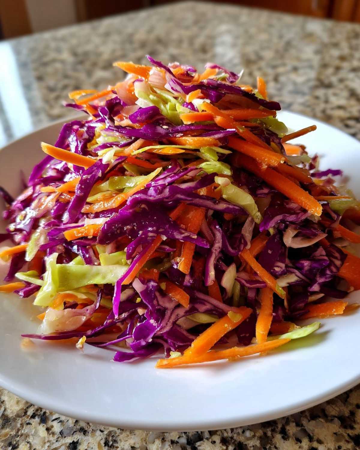 A colorful mound of shredded red cabbage, green cabbage, and carrots making up a fresh cabbage salad.