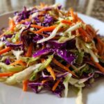 Close-up of a colorful cabbage salad featuring shredded red cabbage, green cabbage, and bright orange carrots.