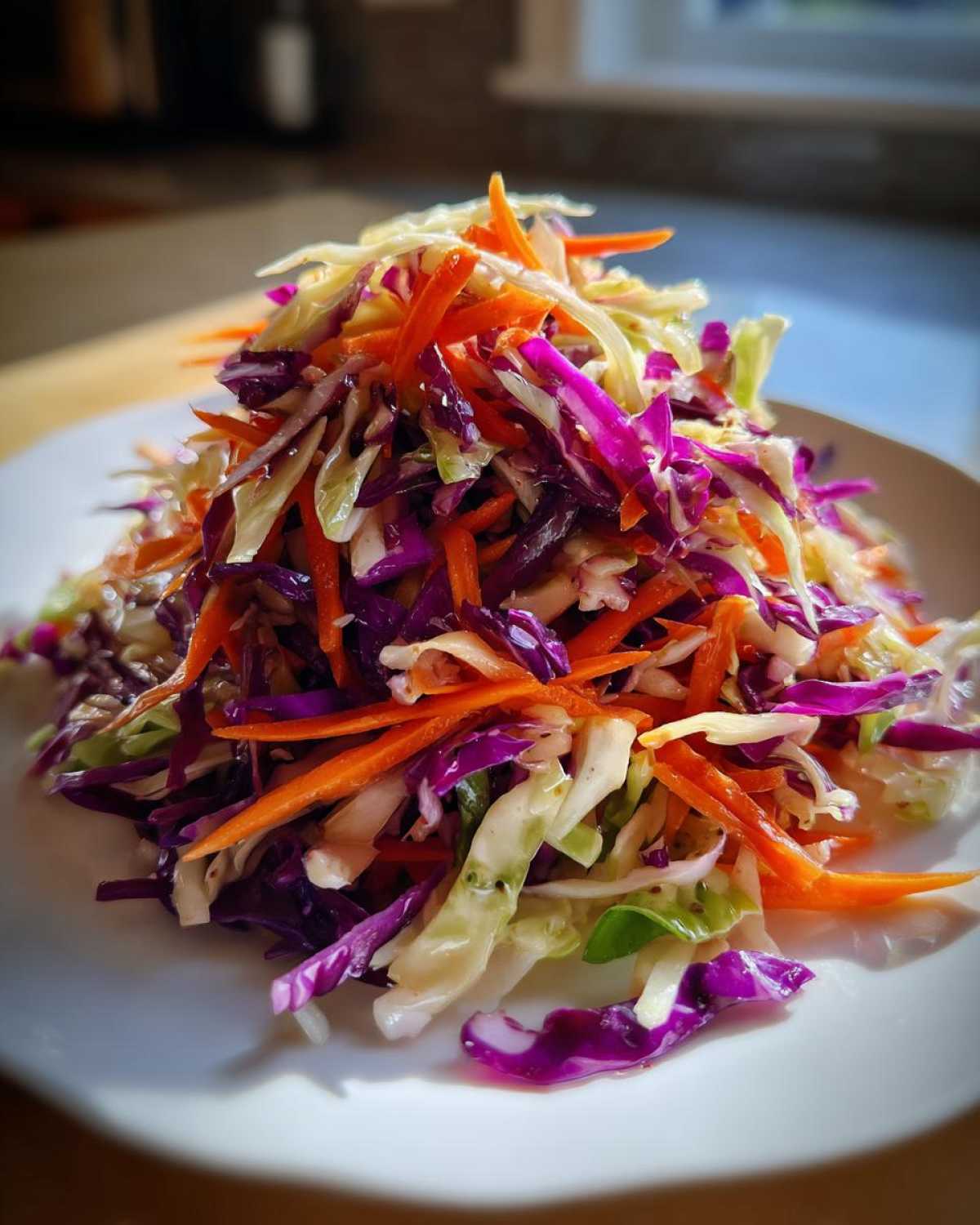 A vibrant mound of homemade cabbage salad featuring shredded red cabbage, green cabbage, and bright orange carrots.