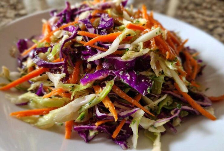 Close-up of a colorful cabbage salad featuring shredded red cabbage, green cabbage, and bright orange carrots.