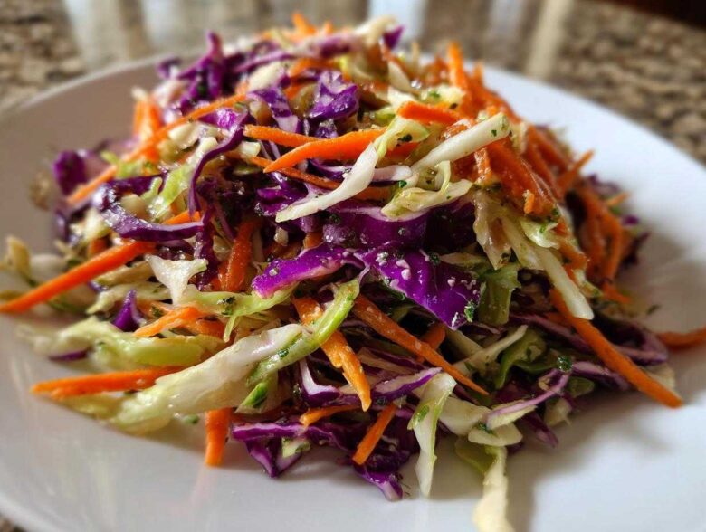 Close-up of a colorful cabbage salad featuring shredded red cabbage, green cabbage, and bright orange carrots.