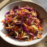 Close-up of a colorful cabbage salad featuring shredded red cabbage, green cabbage, and carrots in a white bowl.