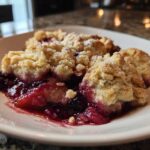 Close-up of a warm serving of berry cobbler with a golden crumb topping dusted with powdered sugar.