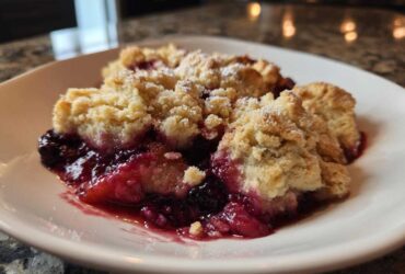 Close-up of a warm serving of berry cobbler with a golden crumb topping dusted with powdered sugar.
