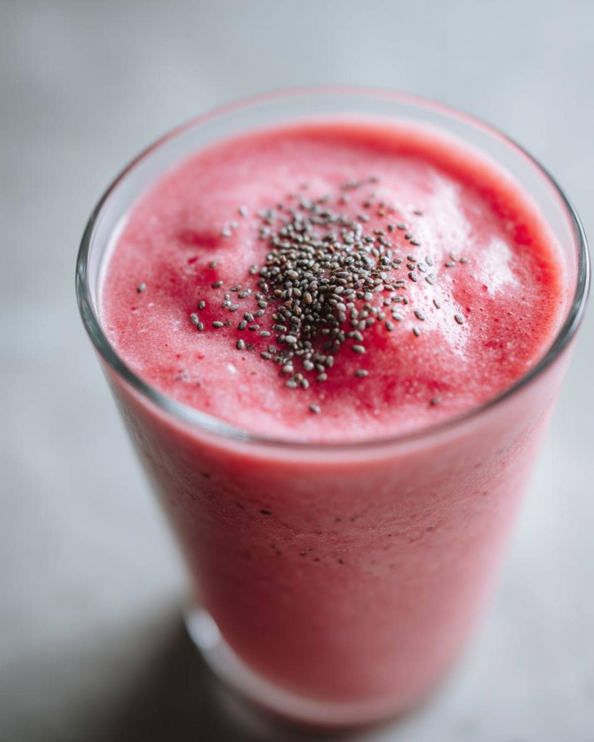 Close-up of a vibrant pink watermelon smoothie in a glass, topped generously with chia seeds.