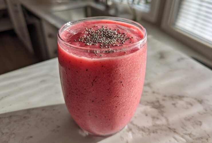 A vibrant pink watermelon smoothie in a glass, topped with chia seeds, sitting on a light countertop.