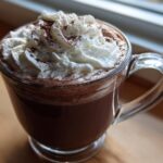 A close-up of rich, dark whipped hot chocolate topped with fluffy whipped cream and cocoa powder.