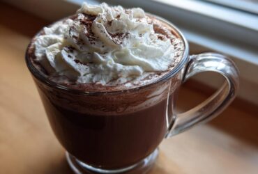 A close-up of rich, dark whipped hot chocolate topped with fluffy whipped cream and cocoa powder.