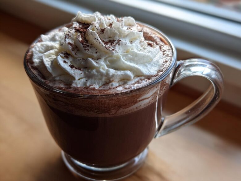 A close-up of rich, dark whipped hot chocolate topped with fluffy whipped cream and cocoa powder.