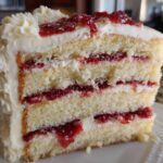 Close-up of a decadent slice of white chocolate raspberry cake showing four layers of sponge, filling, and white frosting.