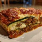 Close-up of a hearty slice of zucchini lasagna featuring layers of meat sauce, ricotta, and zucchini noodles.