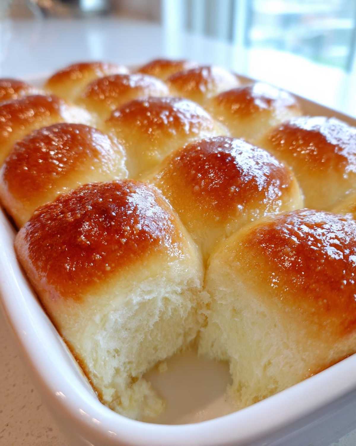 Close-up of golden brown, buttery rolls baked together in a white dish, showing the soft interior texture.