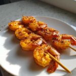 Close-up of perfectly cooked Air Fryer Crispy Cajun Shrimp Skewers seasoned with spices on a white plate.
