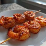 Close-up of several Air Fryer Crispy Cajun Shrimp Skewers arranged on a white plate, showing golden-brown seasoning.
