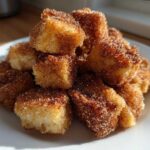 A pile of golden Air Fryer Crispy Cinnamon Sugar Biscuit Bites coated heavily in cinnamon sugar.
