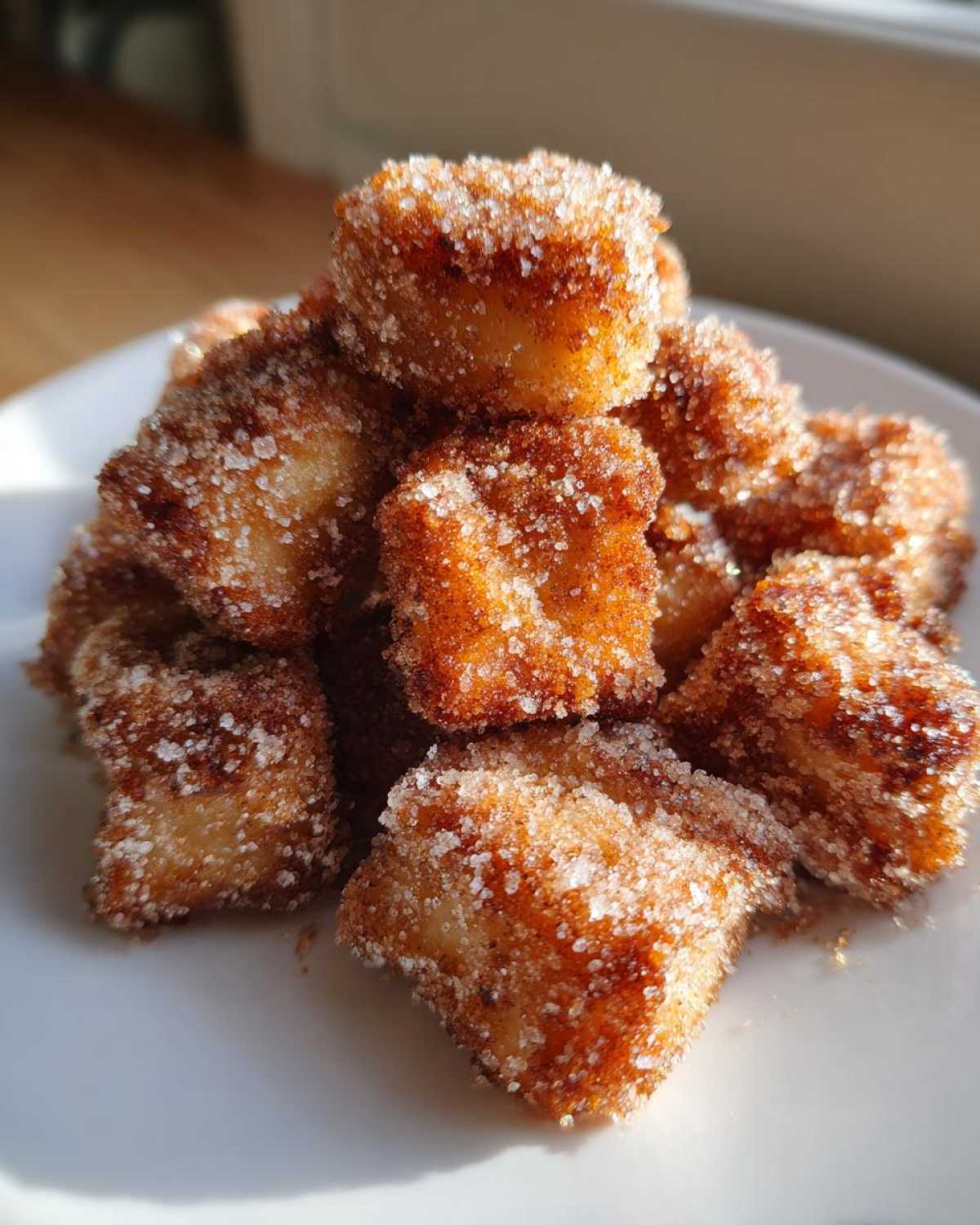 A close-up pile of golden brown Air Fryer Crispy Cinnamon Sugar Biscuit Bites coated heavily in sparkling sugar.