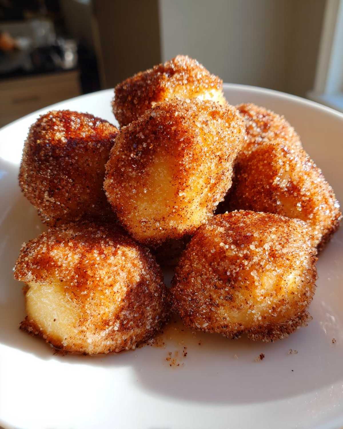 A close-up of several Air Fryer Crispy Cinnamon Sugar Pretzel Bites coated heavily in cinnamon sugar, piled in a white bowl.