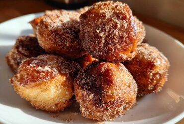 A close-up of several Air Fryer Crispy Cinnamon Sugar Pretzel Bites piled on a white plate, heavily coated in sugar.
