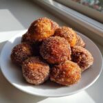 A pile of golden brown Air Fryer Crispy Cinnamon Sugar Pretzel Bites coated heavily in sparkling cinnamon sugar on a white plate.