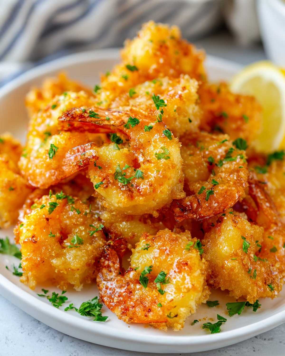 A close-up of a pile of golden brown Air Fryer Crispy Garlic Butter Shrimp garnished with fresh parsley and a lemon wedge.