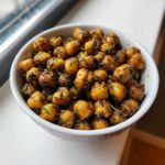 A white bowl filled with golden brown, crispy Air Fryer Crispy Garlic Herb Chickpeas seasoned with visible green herbs.