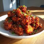 A mound of glossy, saucy Air Fryer Crispy Korean Chicken Bites garnished with sesame seeds and green onions.
