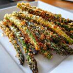 A close-up of Air Fryer Crispy Parmesan Asparagus Fries piled on a white plate, showing golden brown breading.