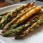 Close-up of golden brown Air Fryer Crispy Parmesan Asparagus Fries stacked on a white plate.