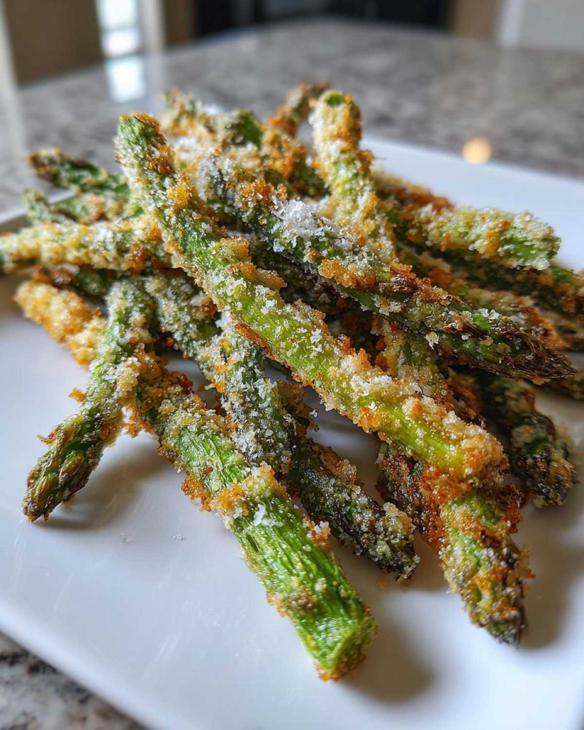 Close-up of Air Fryer Crispy Parmesan Asparagus Fries piled on a white plate.