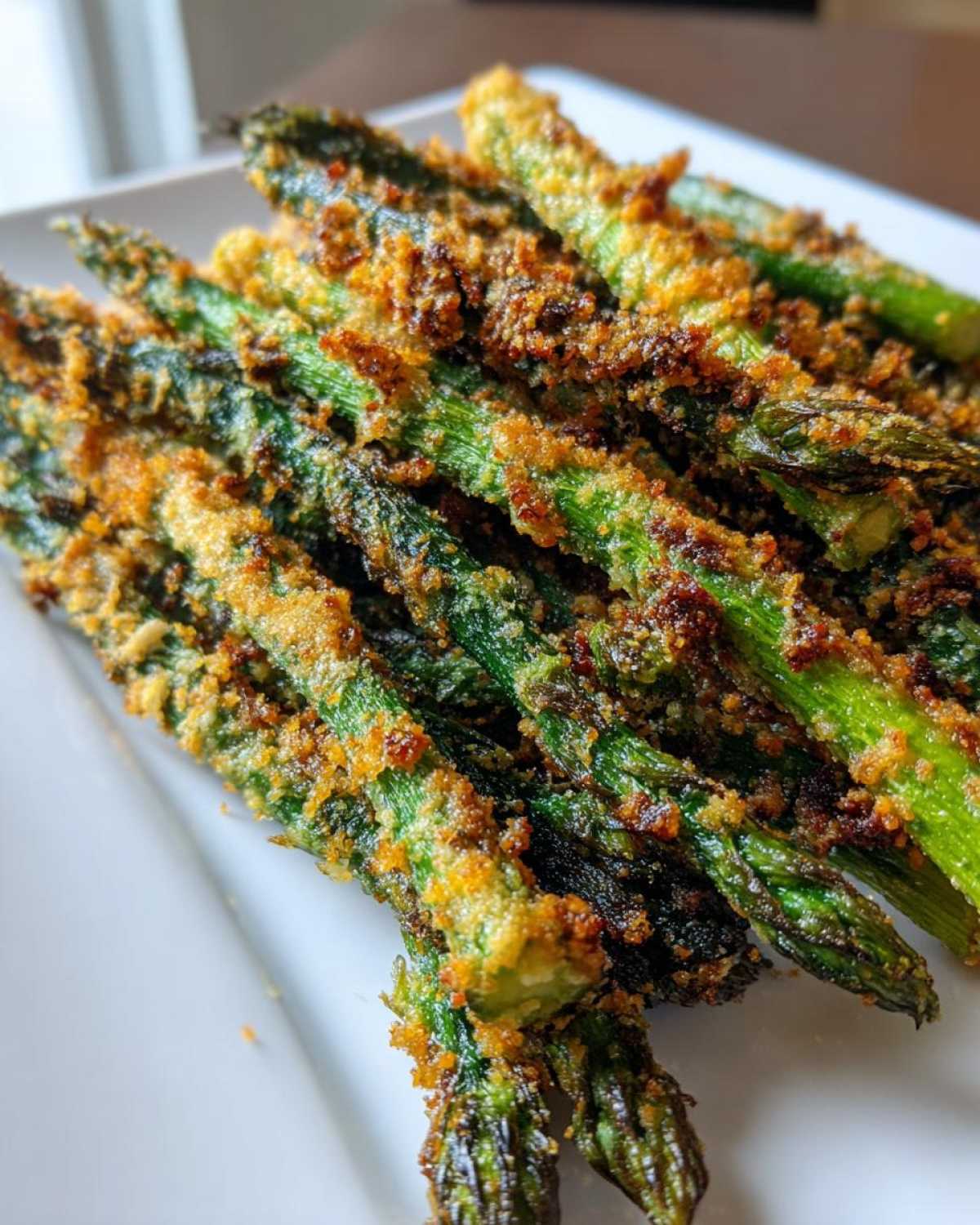 Close-up of Air Fryer Crispy Parmesan Asparagus Fries piled on a white plate, showing a golden, crunchy coating.