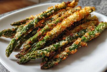 Close-up of golden brown Air Fryer Crispy Parmesan Asparagus Fries stacked on a white plate.
