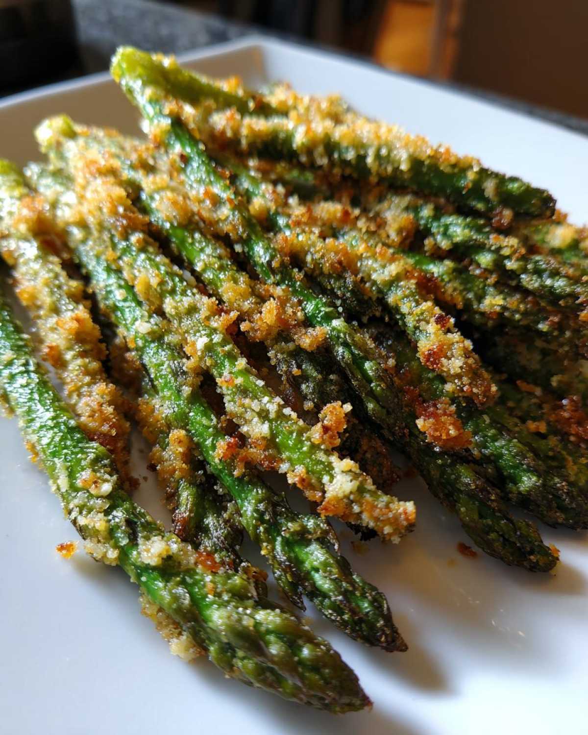 Close-up of bright green Air Fryer Crispy Parmesan Asparagus Fries piled on a white serving dish.
