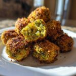 A stack of golden brown Air Fryer Crispy Parmesan Broccoli Tots on a white plate, one is broken open showing the green interior.