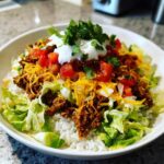 A close-up of a fully assembled Air Fryer Crispy Turkey Taco Bowls with rice, seasoned ground turkey, lettuce, cheese, tomatoes, and sour cream.