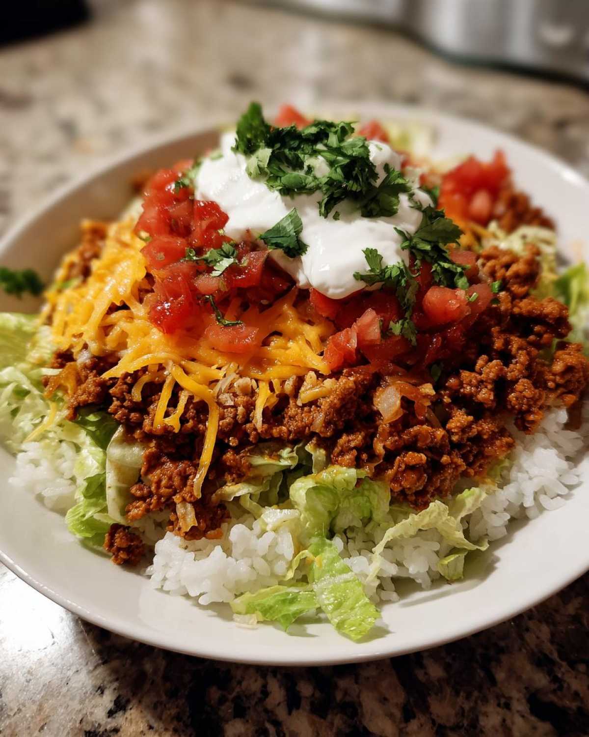 A finished bowl of Air Fryer Crispy Turkey Taco Bowls layered with rice, lettuce, seasoned ground turkey, cheese, tomatoes, and sour cream.