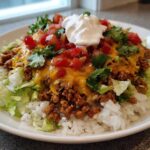 A close-up of a finished Air Fryer Crispy Turkey Taco Bowls featuring rice, seasoned ground turkey, melted cheese, lettuce, tomatoes, and sour cream.