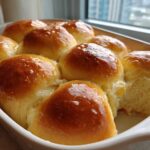 A close-up of golden brown, glossy, buttery rolls baked together in a white rectangular dish.