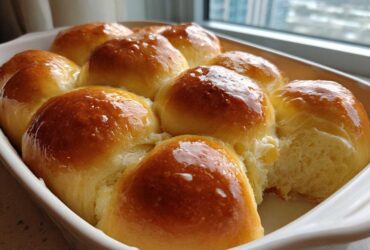 A close-up of golden brown, glossy, buttery rolls baked together in a white rectangular dish.